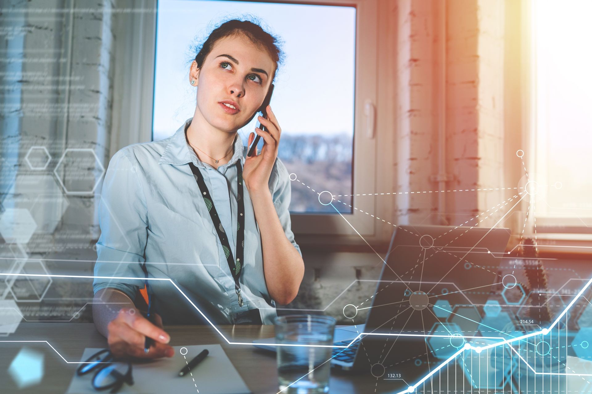 Young attractive casually dressed female entrepreneur answering a call in the office on her mobile phone. Work in process. Virtual futuristic background with various applications icons.